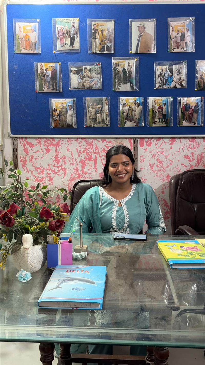 A woman seated at an office desk with a photo display board behind her