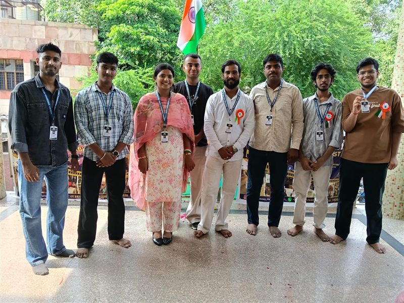 Eight volunteers posing outdoors with an Indian flag behind them